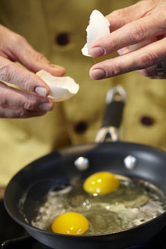 a cook puts cracked eggs in a hot pan
