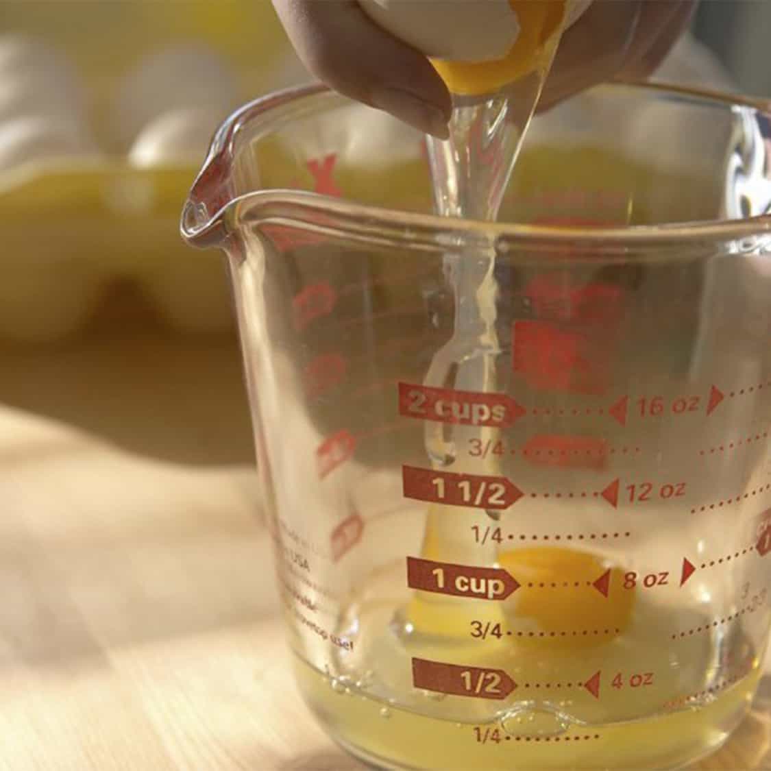 breaking eggs into a glass measuring cup