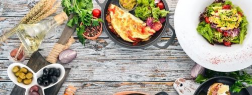 olives, spices, an omelette, and a salad on a wooden table