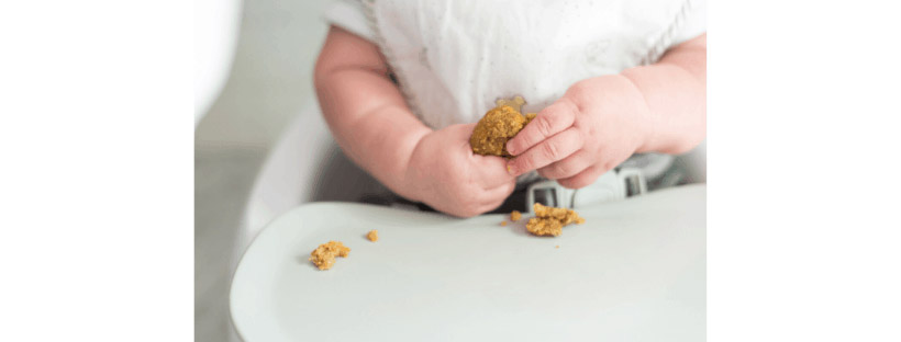 close-up image of a baby sitting in a high chair playing with food