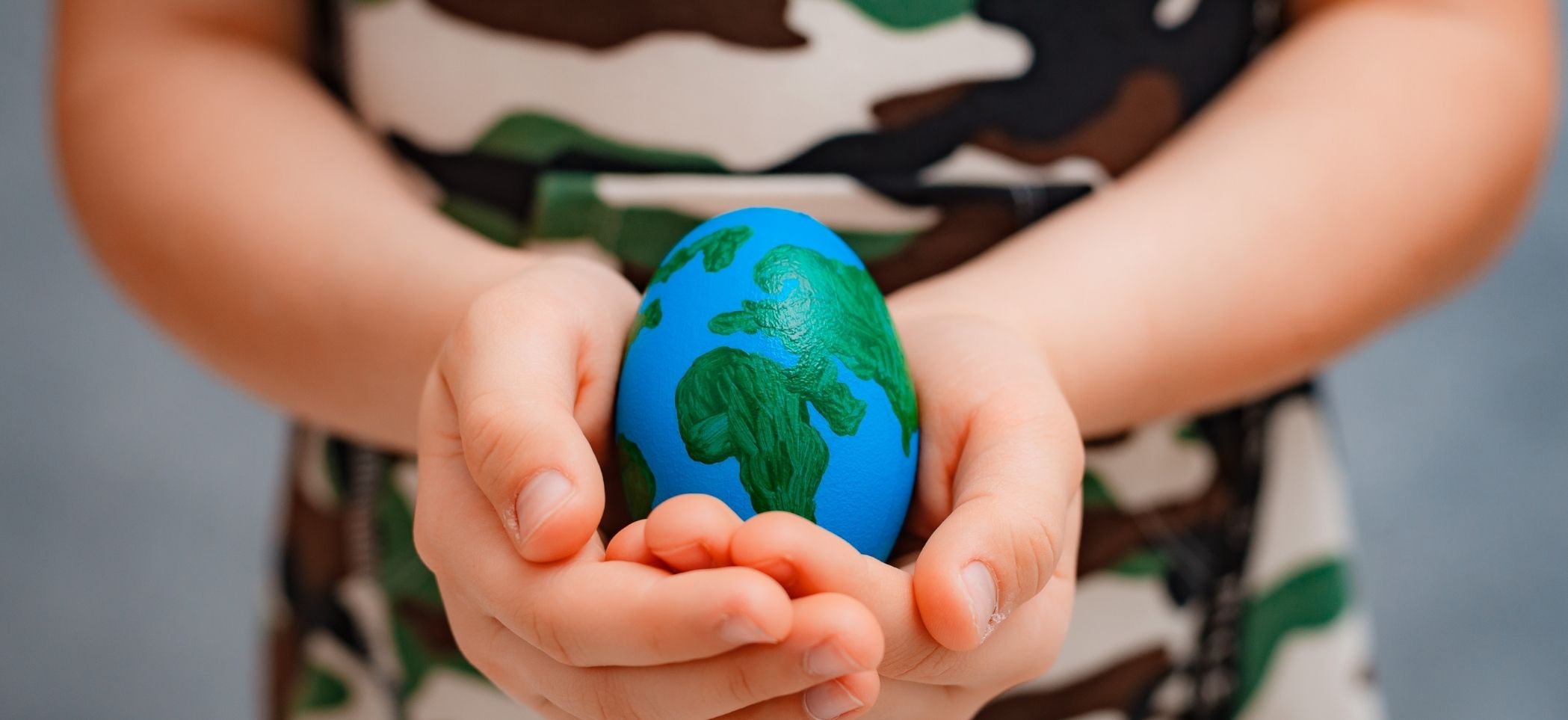 a child holds an egg that is painted like a globe