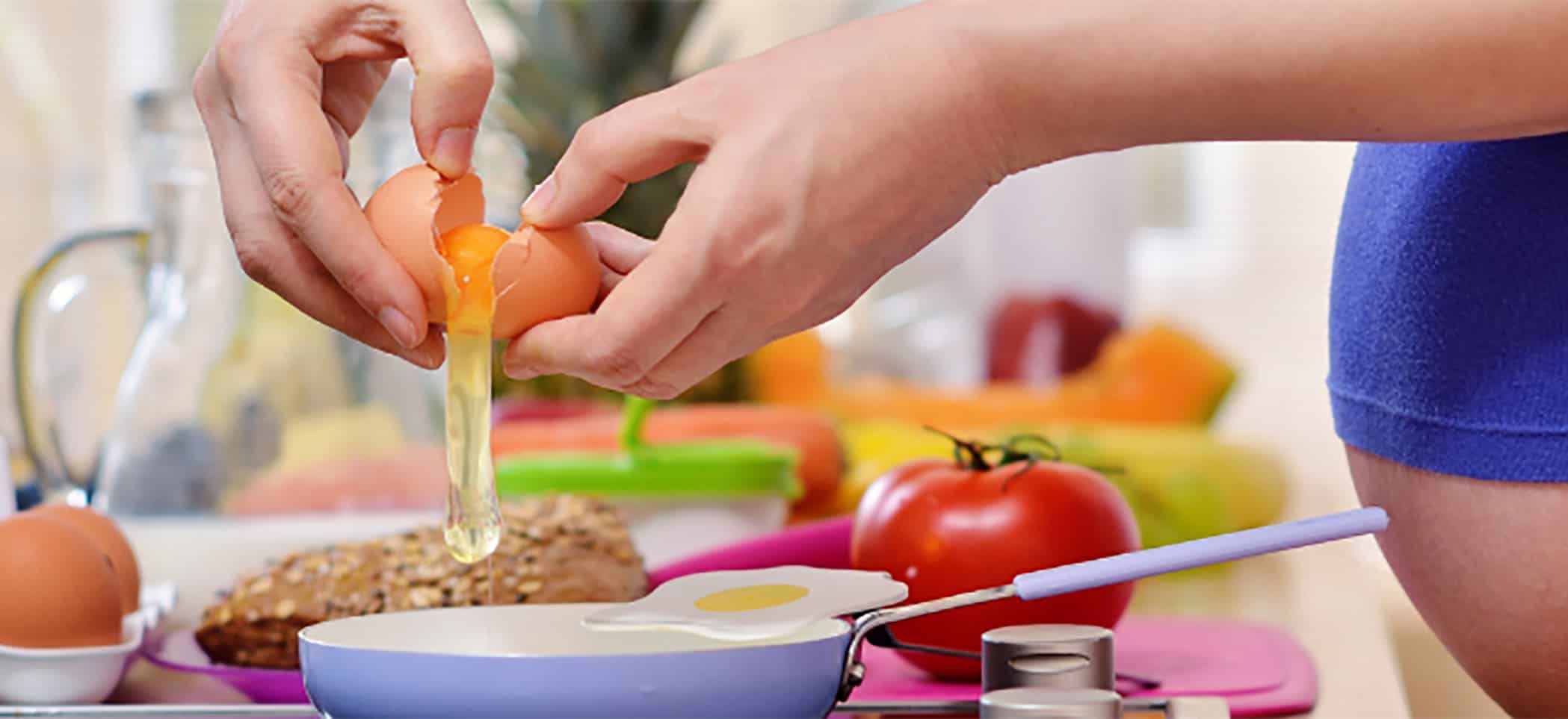 a pregnant person cracks an egg into a frying pan