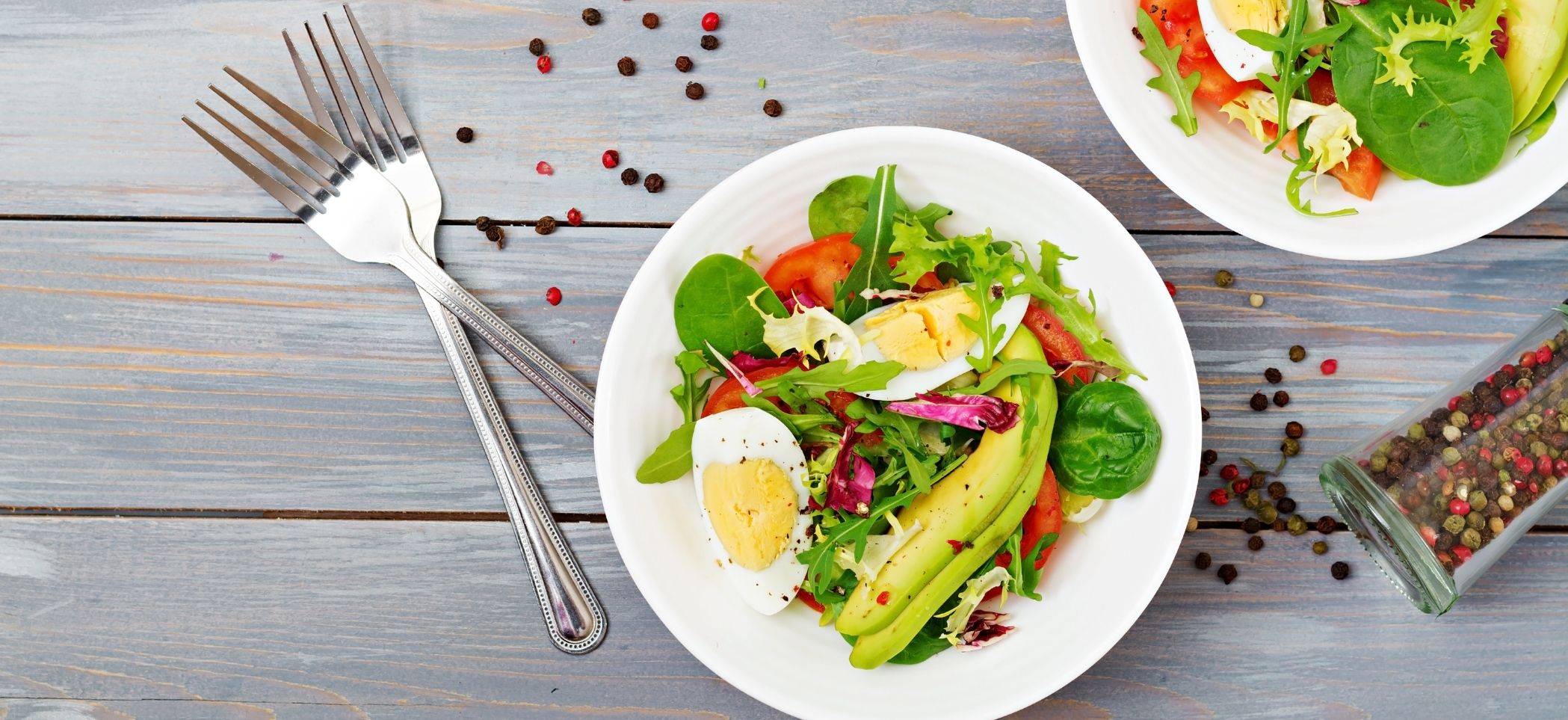 a bowl of salad with avocado, hard-boiled eggs, and peppercorns