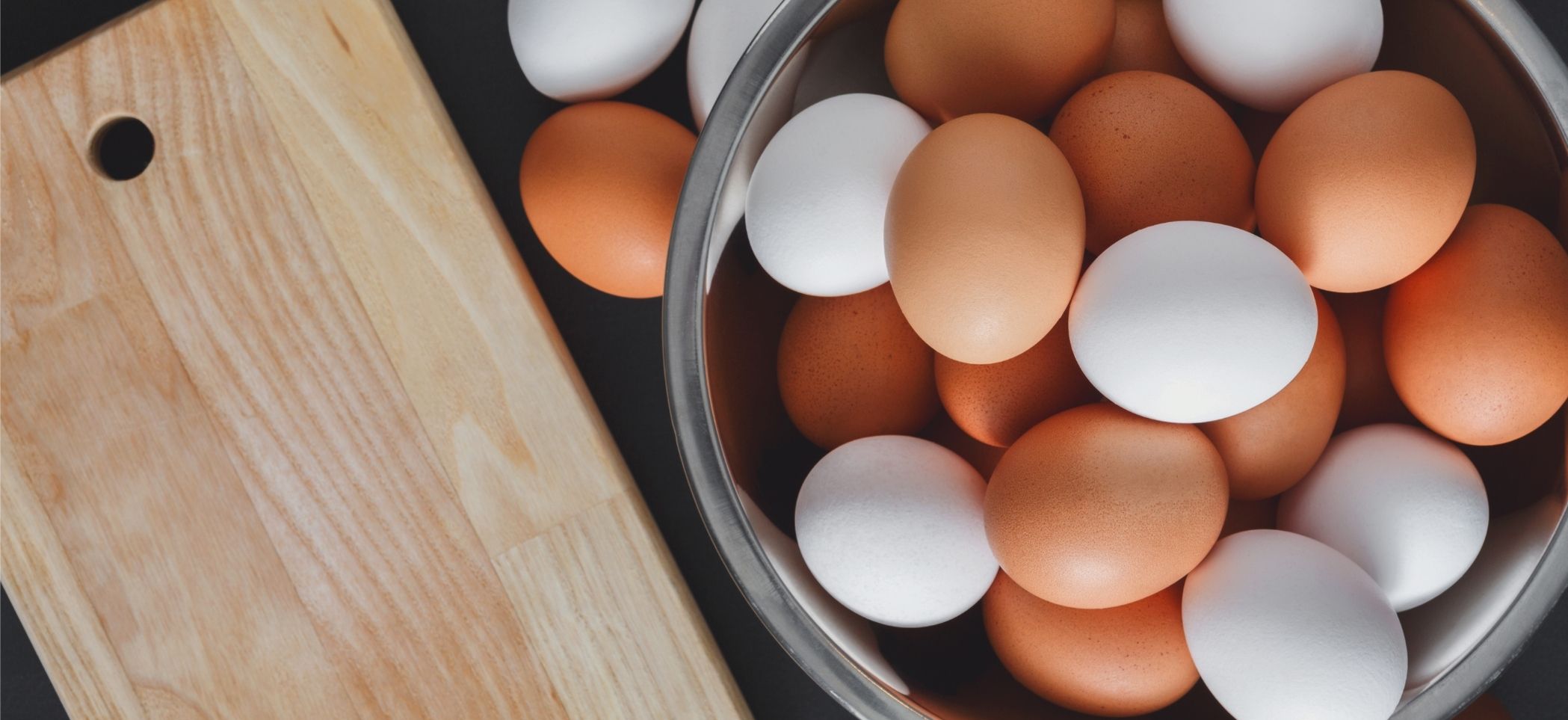 brown and white eggs in a bowl next to a cutting board