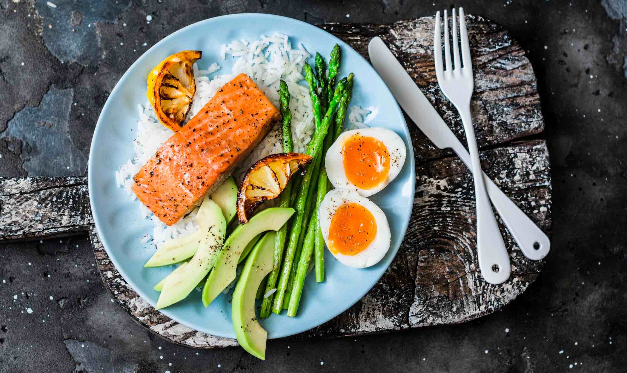 A plate of rice, salmon, avocado, asparagus, and soft-boiled egg