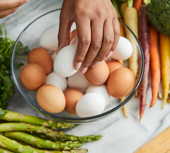 a hand picks an egg out of a bowl of eggs