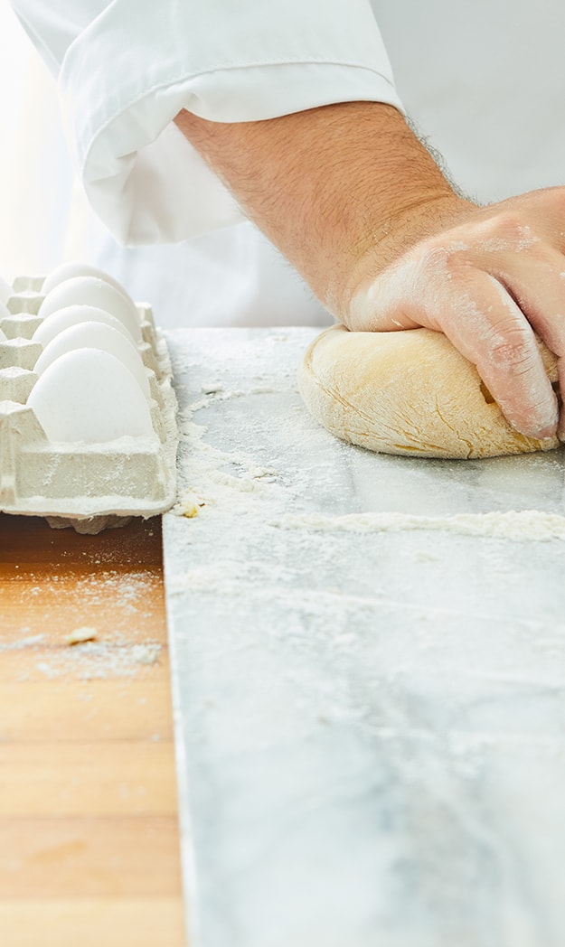 a chef kneads dough next to a carton of eggs