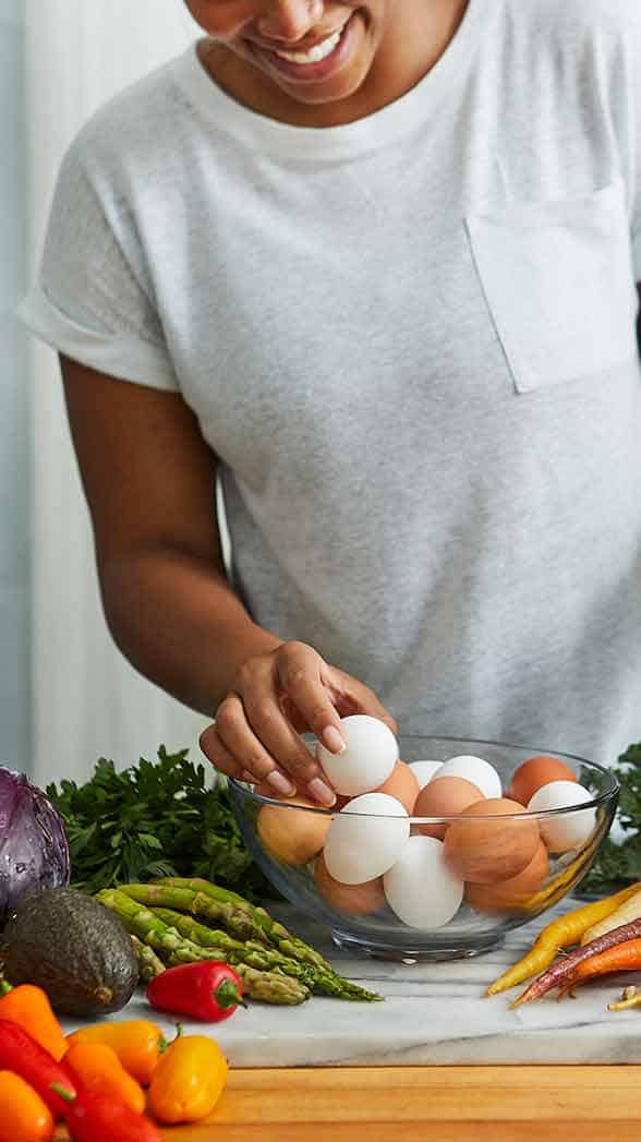 a smiling woman has a bowl full of eggs