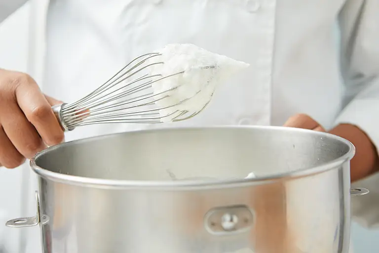 a chef holds a whisk covered in egg whites