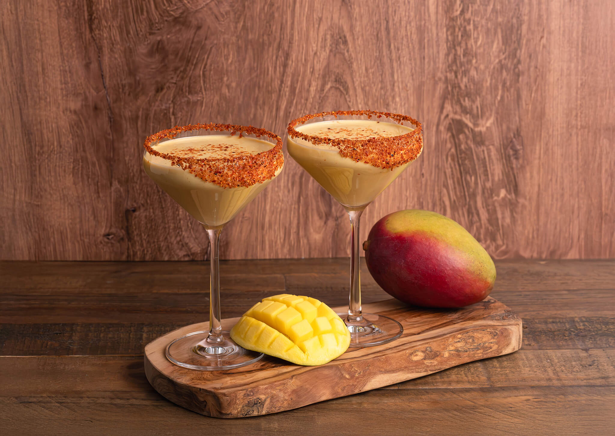 Two glasses of Mango-Chili "Swicy" Nog with Tajín Sugar Rim on top of a wooden board